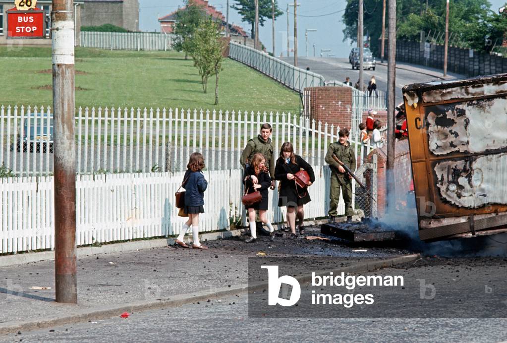 School Children passing infront of British Army Soldiers and Burning Hijacked vehicle, West Belfast during The Troubles, Northern Ireland, 1972