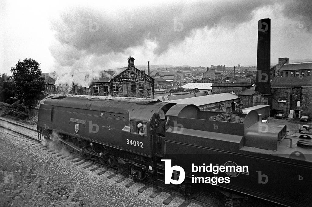 Steam locomotive pulling out of Keighley station against industrial landscape on the heritage Keighley and Worth Valley Railway, West Yorkshire, England, UK, 1989 (b/w photo)