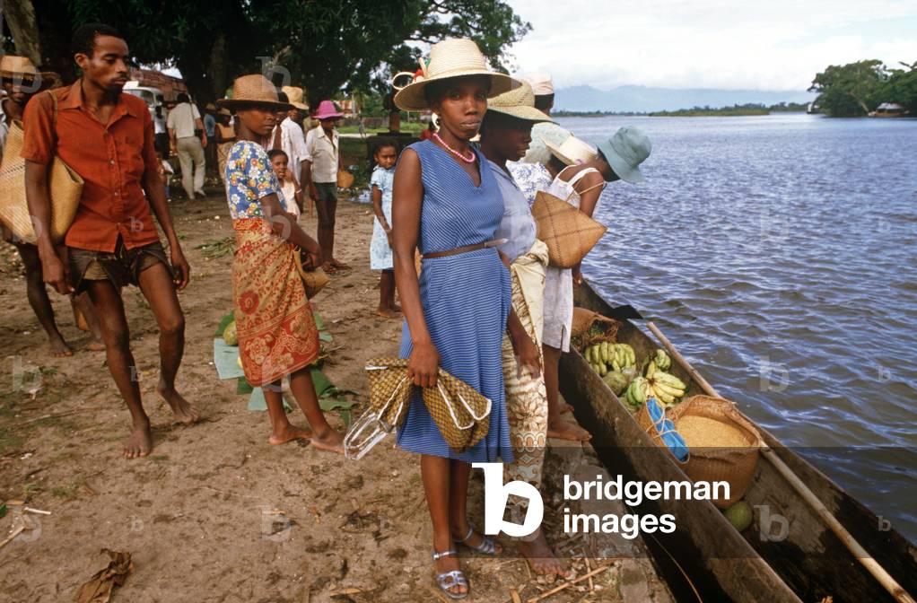 Buying fruit and vegetables and eating a banana from wooden canoes in Maroantsetra, Bay of Antongil, Madagascar, East Africa, Africa, 1980s (photo)