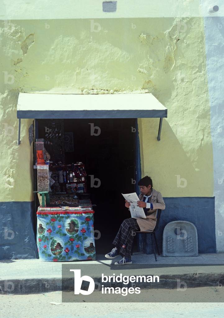 Arab Berger reading newspaper outside tobacconist and sweet shop in South Tunisia, North Africa (photo)