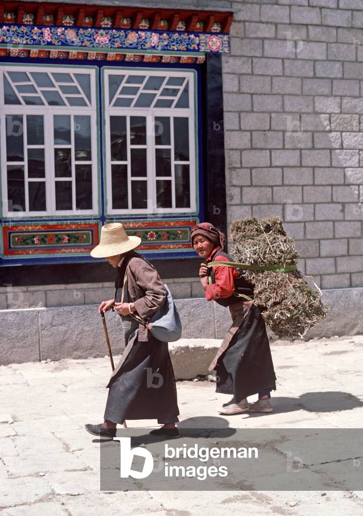 Tibetan women with one of them carrying animal fodder in Lhasa main square (photo)