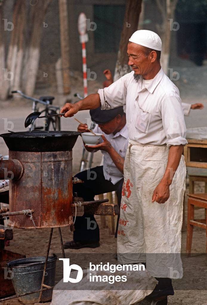 Uyghur cooking in open air kitchen in Turpan market, Xinjiang market, China, 1985 (photo)