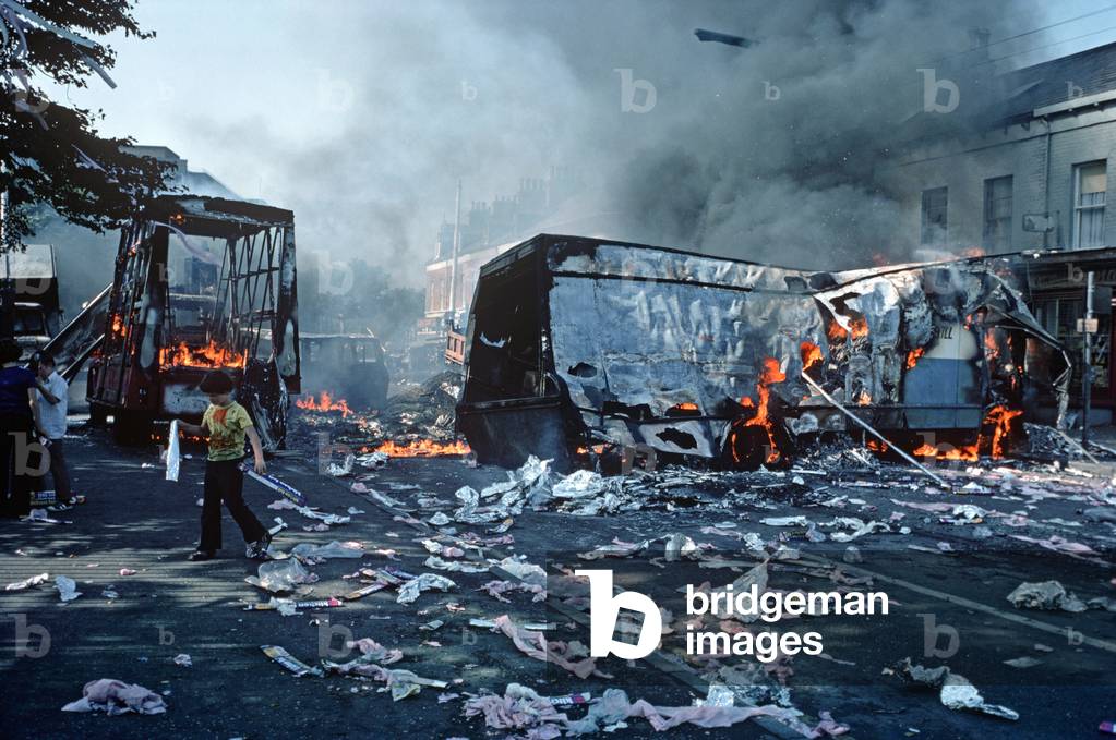 Children playing amongst debris from Hijacked Burning Vehicles after Riots in West Belfast during The Troubles, Northern Ireland, 1976 (photo)