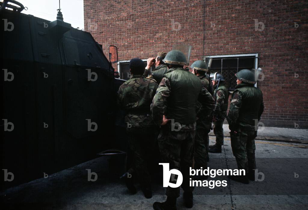 British army soldiers observing incident from behind Saracen personnel carrier during The Troubles, Northern Ireland, 1973