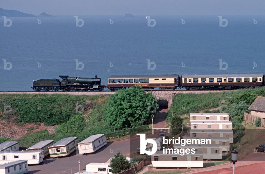 Steam train of the Heritage Dartmouth Steam Railway crossing caravan park with Tor Bay in the background, Devon, England, UK, 1989 (photo)