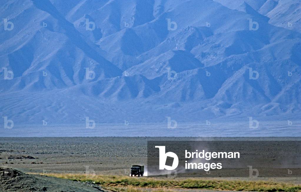 Truck driving through Gobi desert with Gobi-Altai Mountains in background, Mongolia, Asia