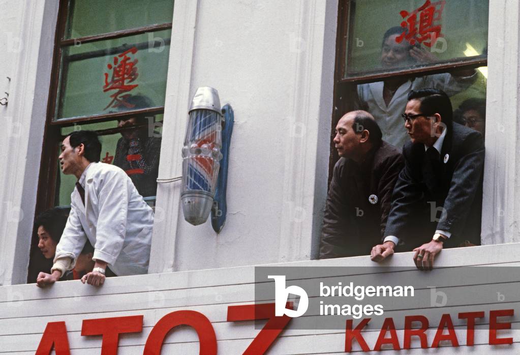 Chinese watching Chinese New Year in Chinatown from upstairs hairdresser and barber window, Soho, London, UK, 1981 (photo)