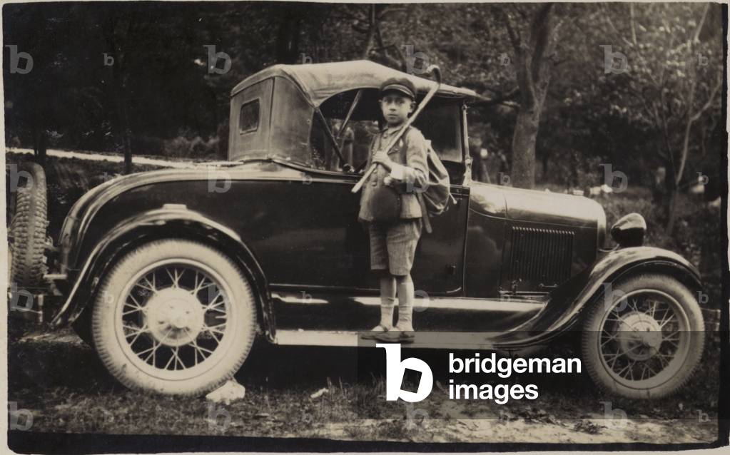 Boy standing on the running board of a car, with hiking gear and a walking stick, near Shumen, Bulgaria, 1936 (b/w photo)