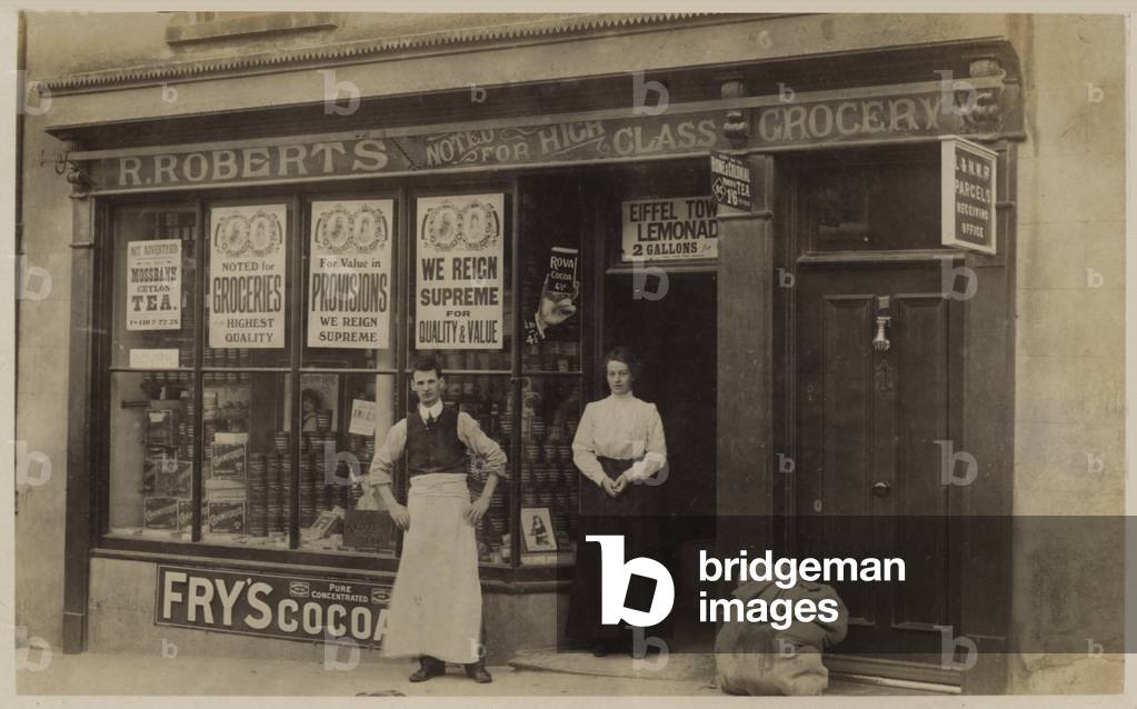 Man and woman outside their grocer's shop (b/w photo)