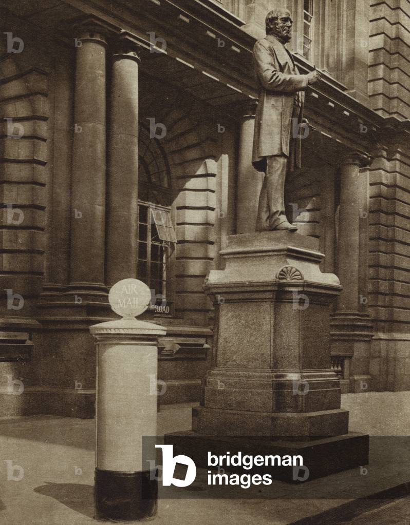 Statue of Rowland Hill, founder of the modern postal service in Britain and inventor of the postage stamp, outside the General Post Office, London, next to a blue air mail pillar box (b/w photo)