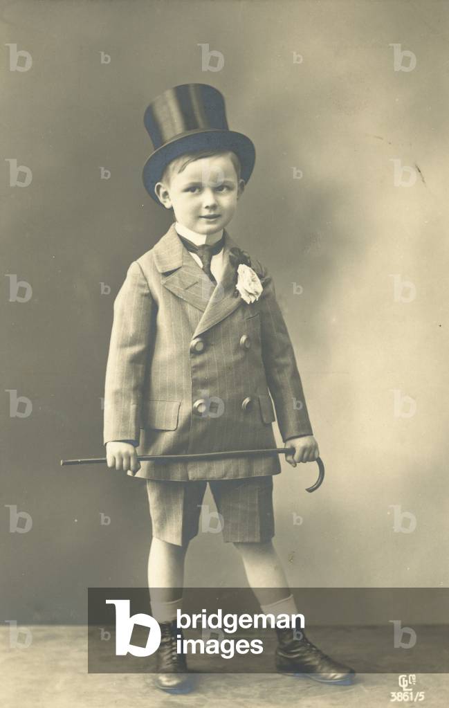 Boy in double-breasted suit, wearing a top hat and holding a cane (b/w photo)