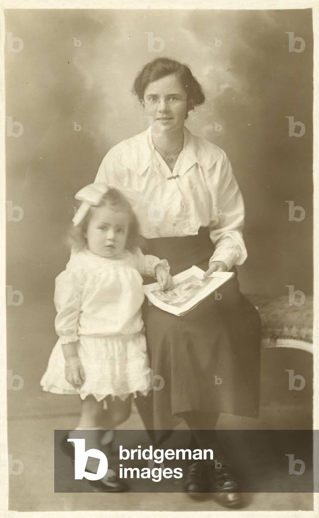 Pretty girl, mother or governess, showing photos to young child (b/w photo)
