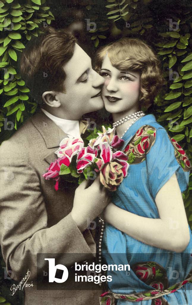 Man, carrying flowers, kissing pretty girl on the cheek (colour photo)
