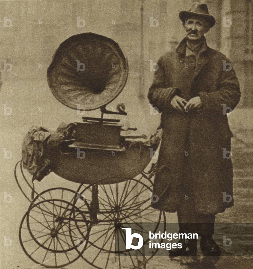 Man with a gramophone mounted on a pram on Holborn at Christmas (b/w photo)