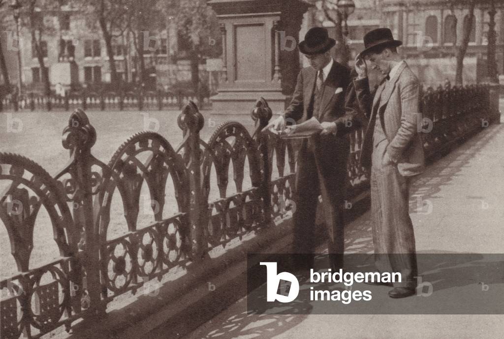 Officers of the Ministry of Works and Planning discussing the removal of iron railings in Parliament Square, London, to be used as scrap metal for the manufacture of steel, World War II (b/w photo)