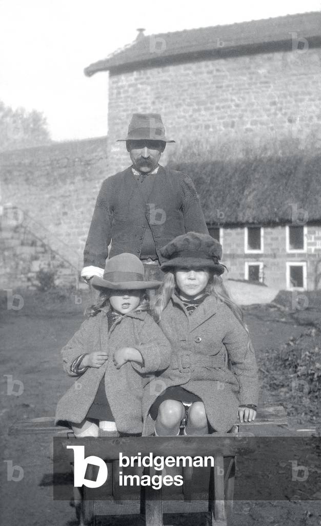 Two little girls sitting in a wheelbarrow, pushed by a servant. Brittany (France), photography, 1919-1920.