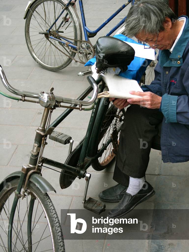 Street scene, old man reading near his bike, Pekin, China, 2006.