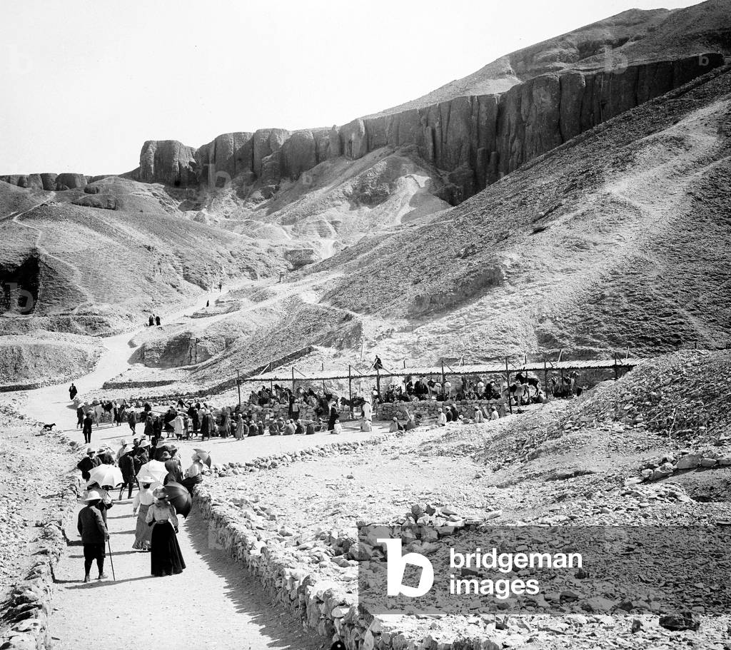 Egypt: Cook cruise, tourists with umbrella and colonial helmet head to mullet shelters and porter chairs at the foot of the Valley of the Kings, 1900