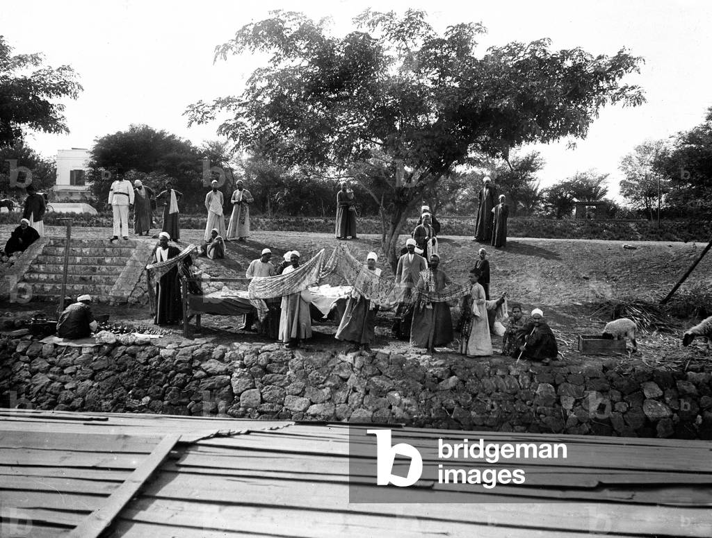Egypt: Cook cruise on the Nile, has a stage, on the bank, merchants offer fabrics and souvenirs to tourists under the watchful eye of a policeman, 1900