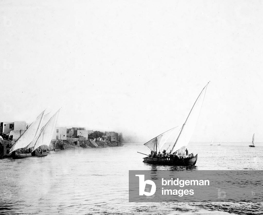 Egypt: Cook cruise, village on the edge of the Nile, off a village, a felouque passenger and cargo transport crosses the cruise ship of tourists, 1900