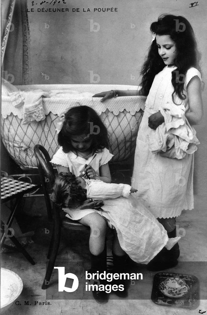 France: gender photo of two little girls giving food to their dolls, 1900