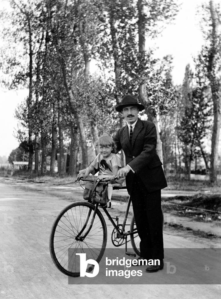France: A man carries his child on a bicycle on a wooded road, 1920