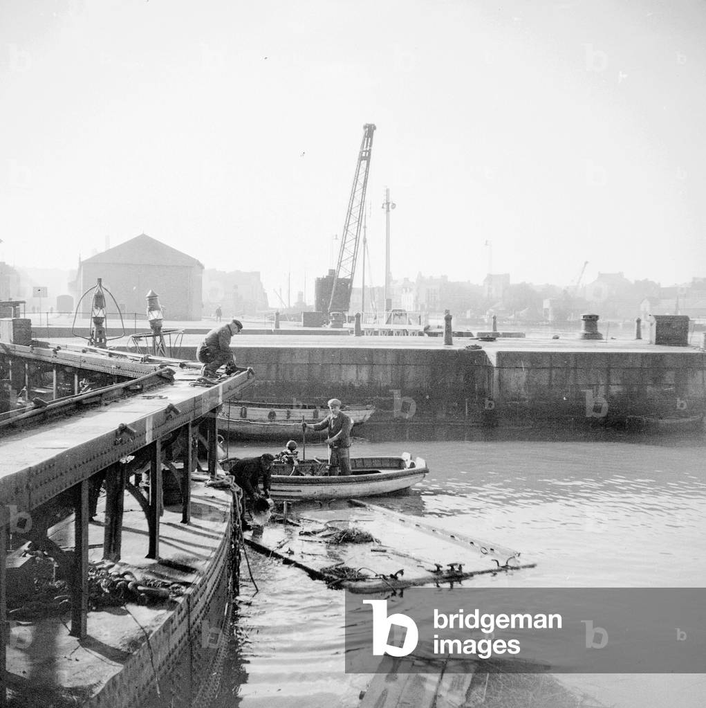 France, Pays de la Loire, Loire-Atlantique (44), Saint-Nazaire (Saint Nazaire): the shipyards, on the lock, 2 workers supply equipment brought by a boat between beacons, 1936