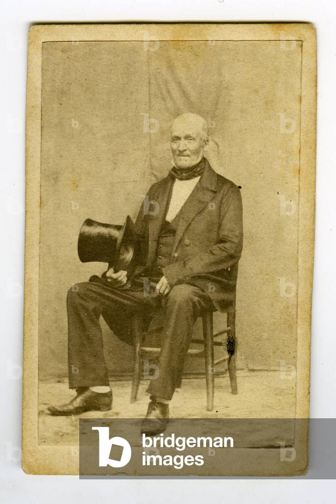 France, A man poses in a makeshift studio with a top hat and a provincial suit, 1865