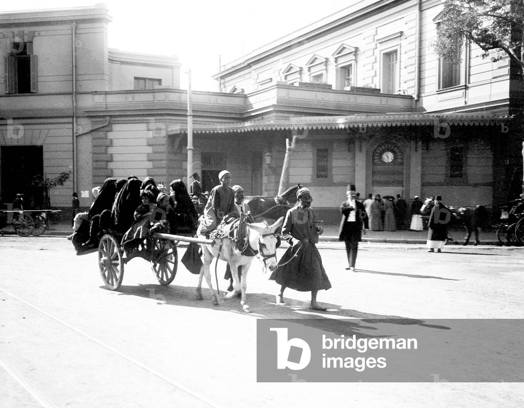 Egypt, Cairo: Cook cruise on the Nile, an Egyptian, carries on a cart pulled by a donkey, about ten women veiled in melaya on an avenue in the European quarter near the railway station, 1900