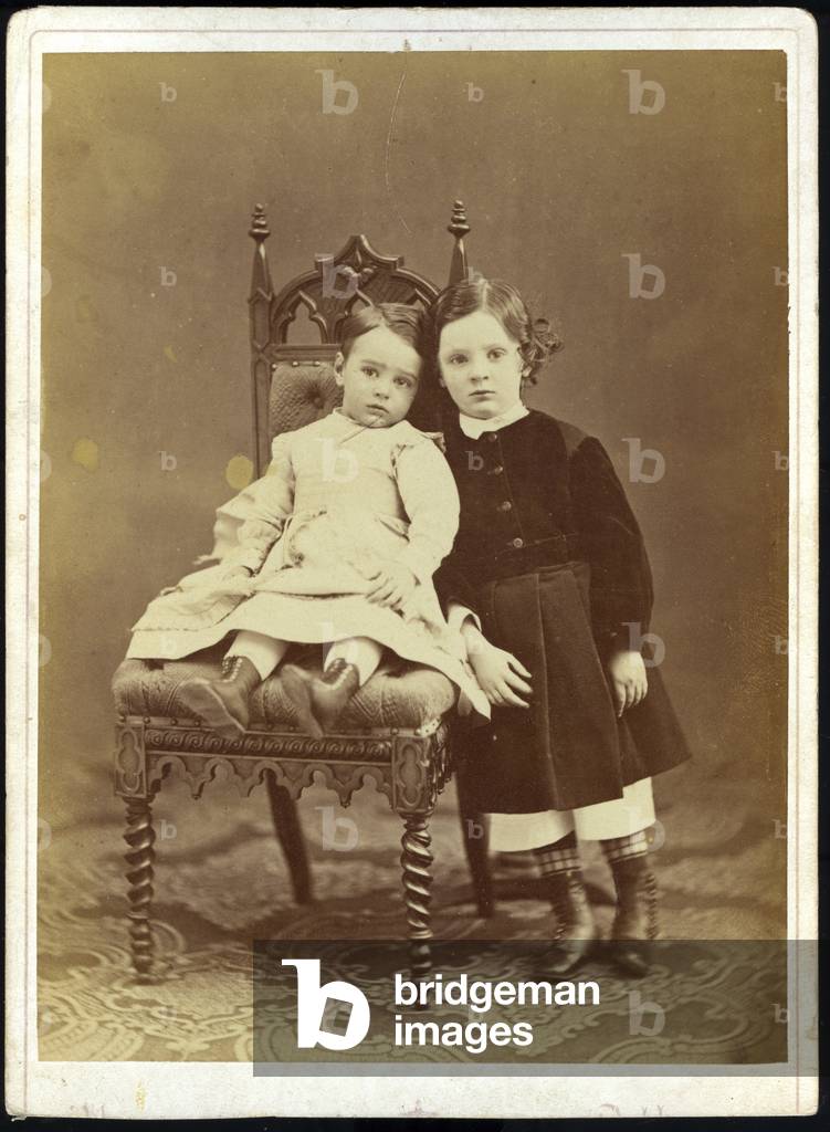 Two children pose in the studio on a neo-Gothic chair, 1865