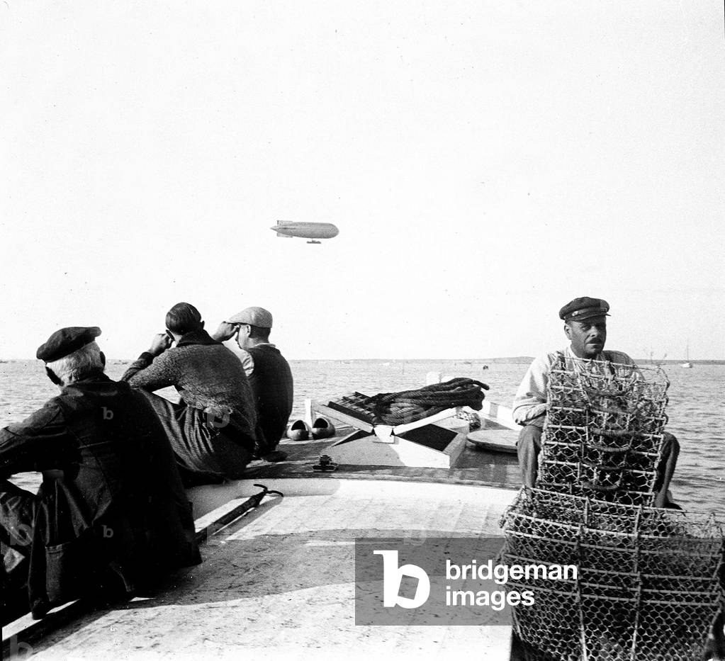 France, Aquitaine, Gironde (33), Arcachon: fishermen in their boat look at an airship balloon, Astra-Torres in the sky, 1935 - zeppelin