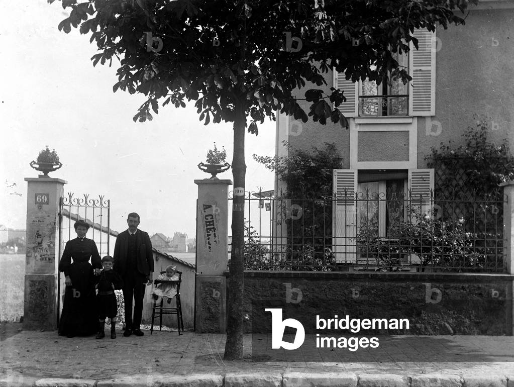 A couple and their two children pose in front of a suburban house, 1910