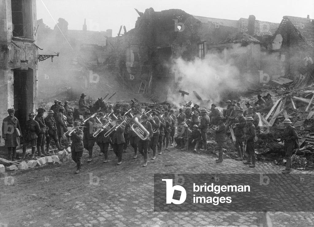 The Band of the 5th Australian Infantry Brigade, led by Bandmaster Sergeant A Peagam of the 19th Battalion, passing through the Grande Place (Town Square) of Bapaume, playing the 'Victoria March', Bapaume, France, 19 March 1917 (b/w photo)