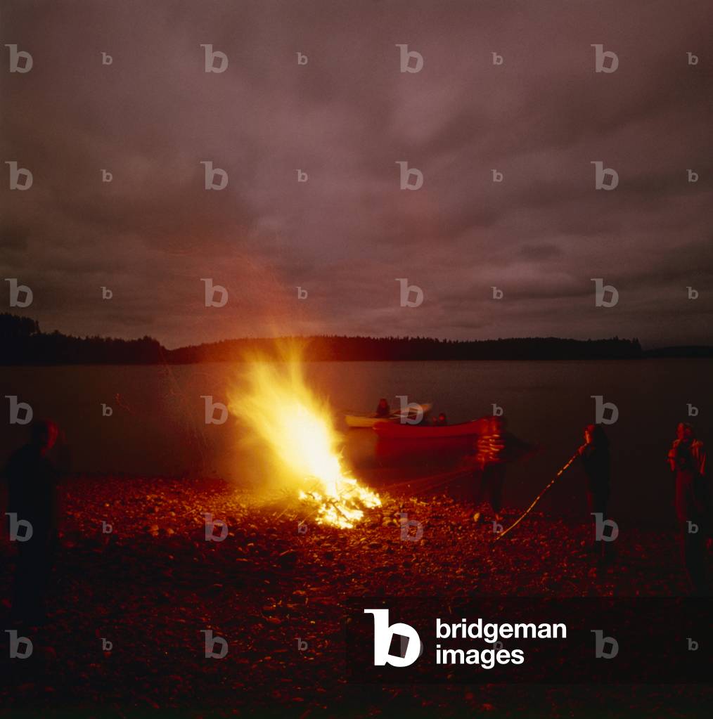 A bonfire by the lake lighting the night on 24th of June, the day of the summer solstice and the feast of Saint John, Finland, 1960s (b/w photo)