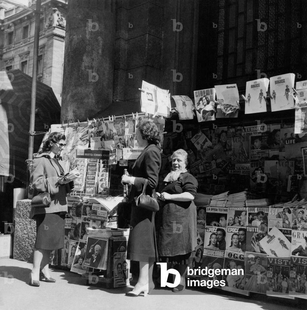Three women near a newspaper kiosk