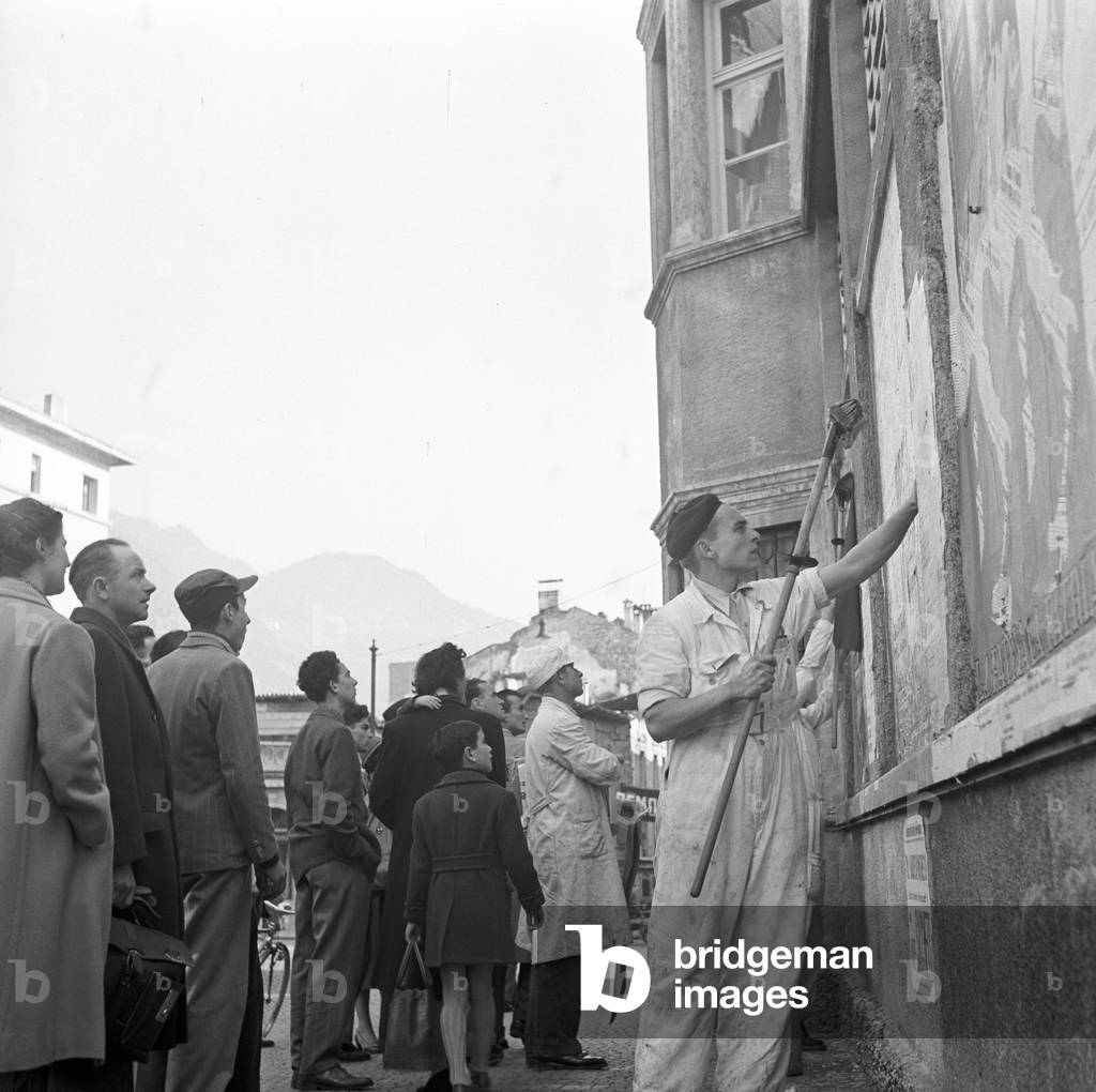 A bill sticker sticking up electoral posters during the regional election in Trentino-Alto Adige/Sudtirol, Italy, November 1952 (b/w photo)