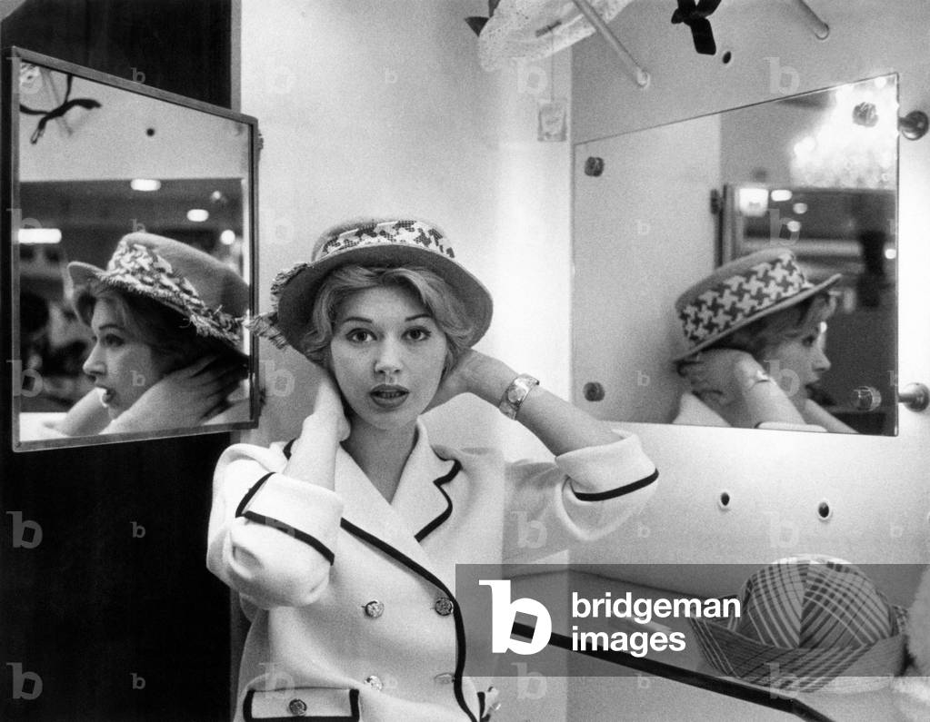 A young woman trying on a hat, Italy, 1959 (b/w photo)