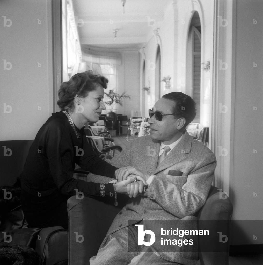A woman holds the hands of a man seated on an armchair