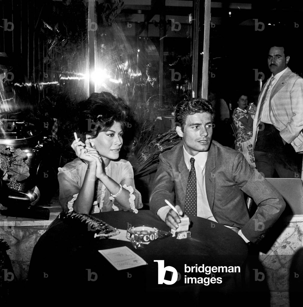 Franca Bettoja and Nino Castelnuovo smoking at a party, Rome, Italy, 1961 (b/w photo)