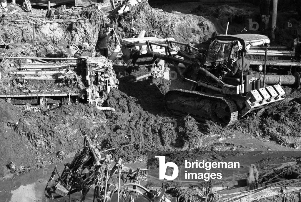 A man moving the rubbles on a bulldozer after a flood in the district of Biella, Italy, 1968 (b/w photo)