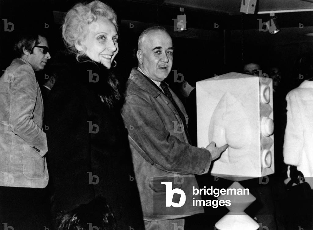 Piero Fornasetti with one of his works, Italian painter and sculptor pointing out a sculpture and having fun. 1988 (b/w photo)