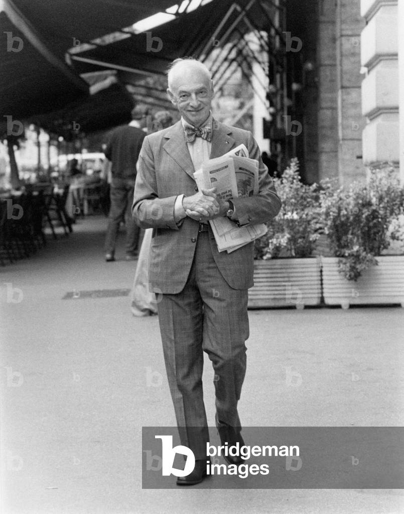 Writer Saul Bellow strolls carrying some newspapers under his arm