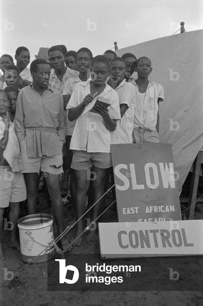 Children waiting for the cars running the East African Safari Rally at a block, Kenya, April 1965 (b/w photo)