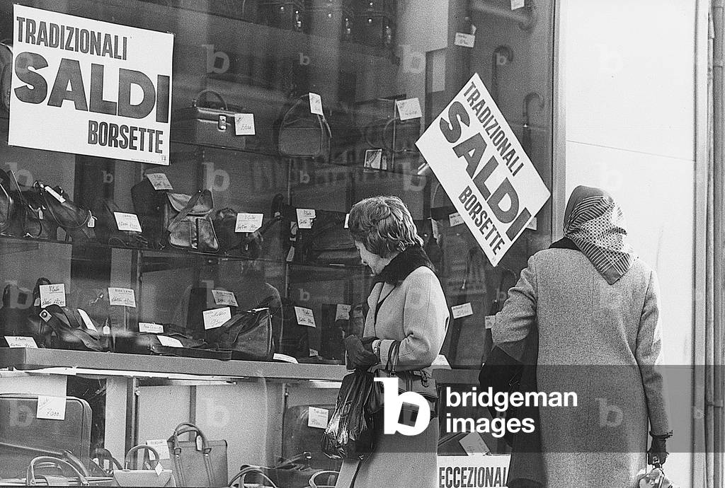 Women watching the window of a leather goods shop displaying goods on sale, Milan, January 1973 (photo)