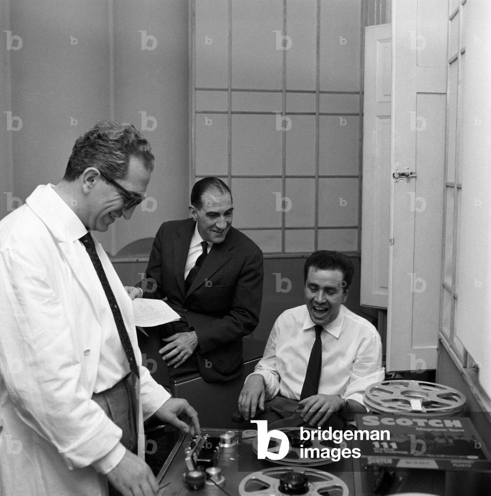 Enzo Tortora smiles while sitting in a radio studio with a colleague and a technician