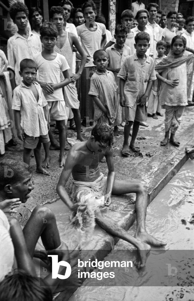 A boy washing himself on a street, Kolkata, India, 1962 (b/w photo)