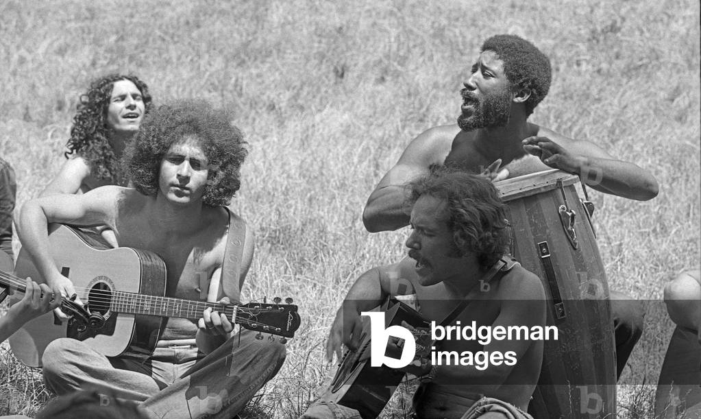 Sitting on the grass, three youngs play a song with guitars and conga, Milan, Italy