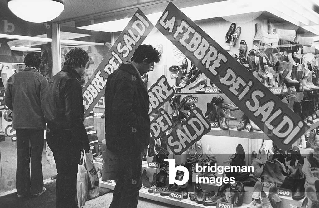 Men watching the window of a shoe shop displaying goods on sale, Milan, 1979 (photo)