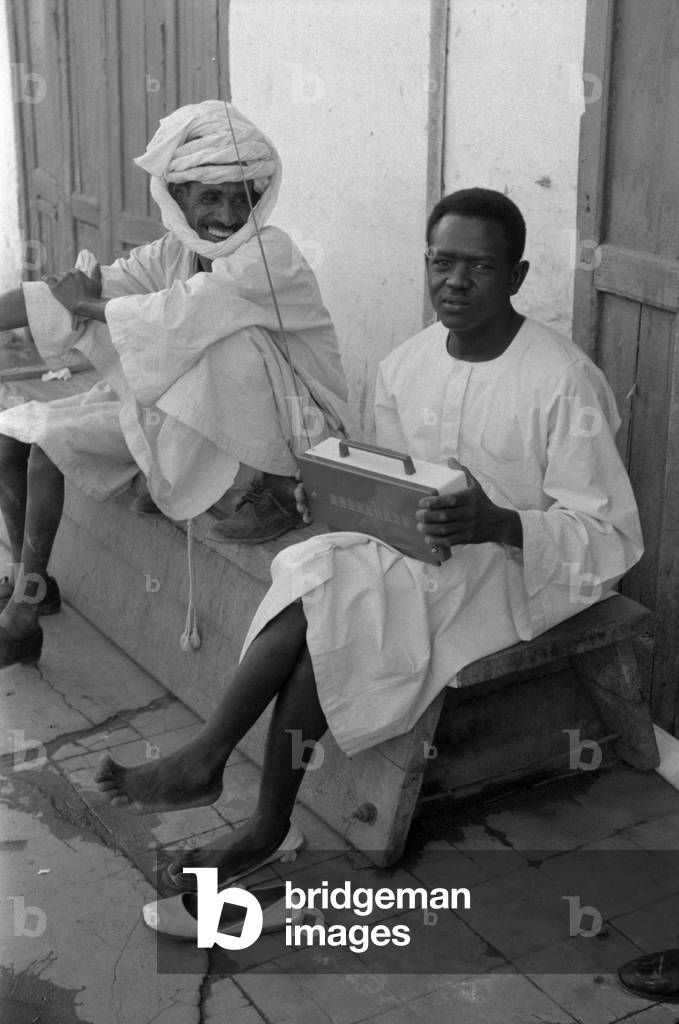 Two Sudanese men sitting in the street and listening to some music, Khartoum, April 1965 (b/w photo)