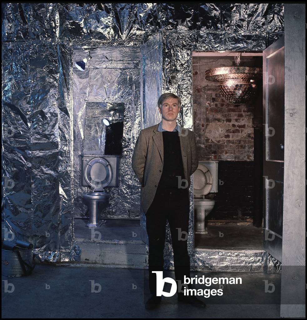 The American painter and director Andy Warhol posing in his studio in front of two toilets.
